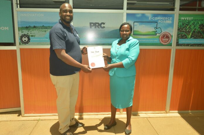 Brian Gacari, CEO PRC issuing s title deed to a happy client - Bizna