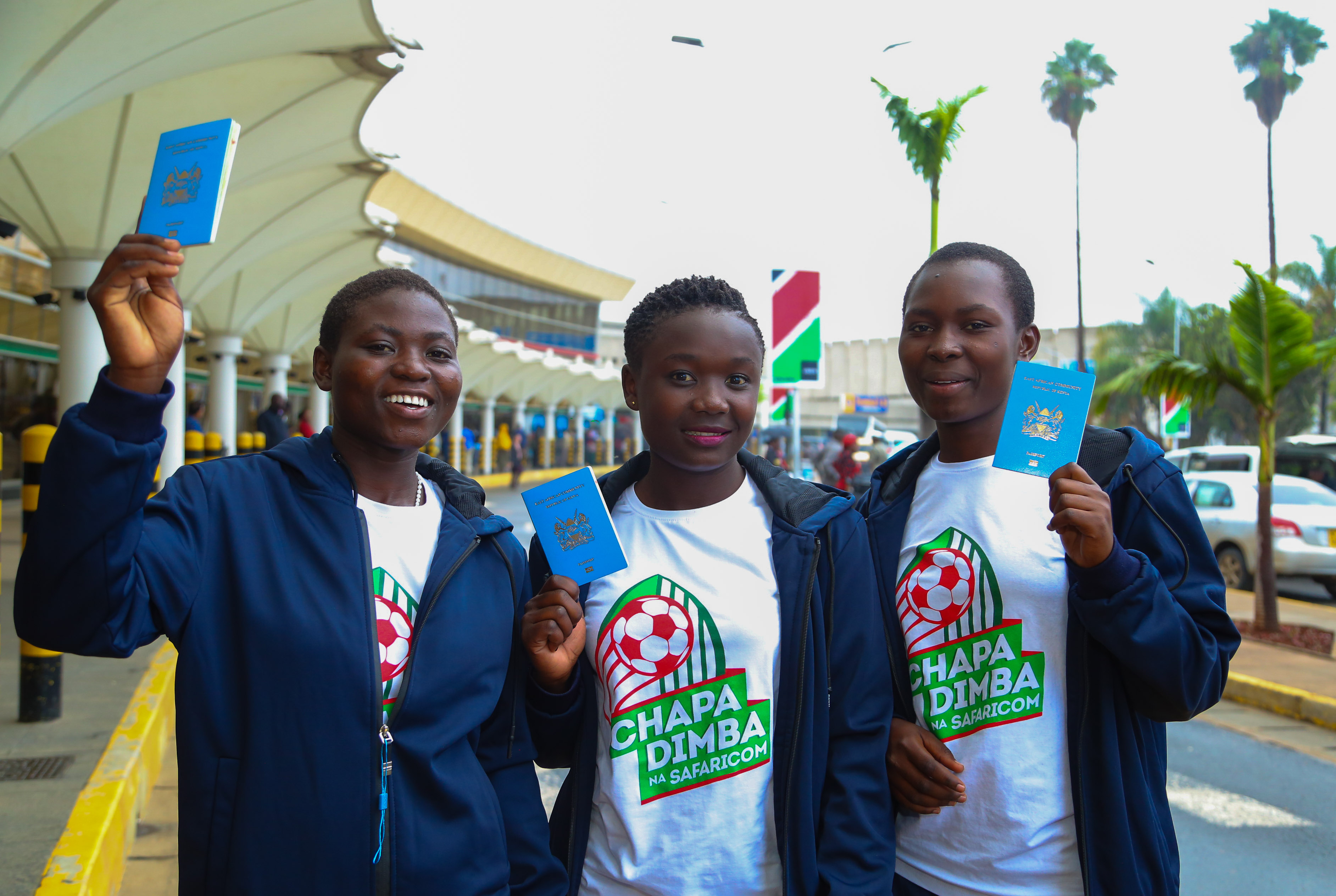Safaricom Chapa Dimba Winners; Plateau Queens players Mary Okumu (Left), in company of her mates Jovyntine Simbe and Christine Awuor express their enthusiasm on a photo-call, vibrantly displaying their passports ahead of their travel to London at the Jomo Kenyatta International Airport - Bizna 