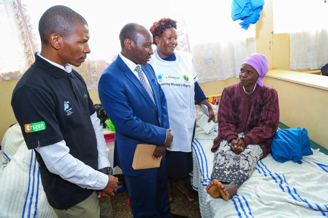 Safaricom HOD Regional Sales and Operations- Mount Kenya Region, George Mbyuki (left), with Embu County CEC Health, Dr. Jamleck Muturi, talk to 50- year- old fistula patient, Jane Gacheru, a mother of five from Wiyumirirye. Also present is Shelmith Mwangi, a trained fistula nurse.