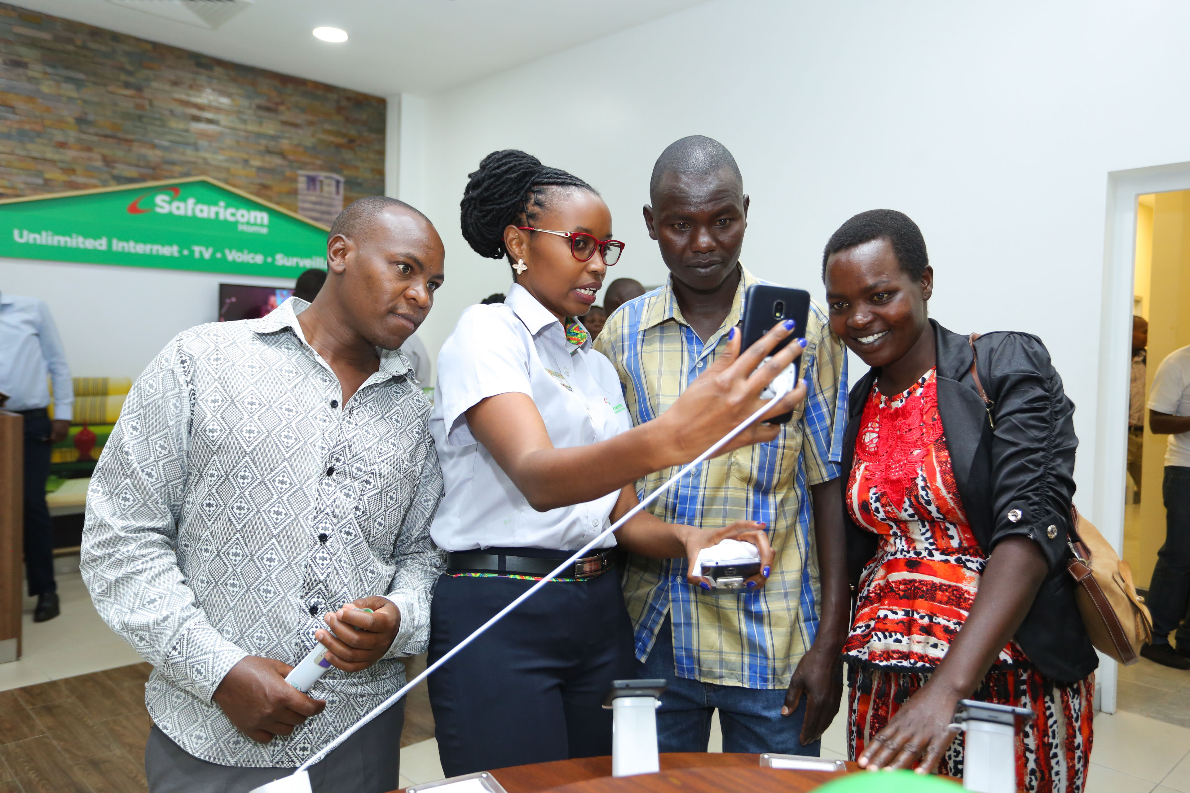 Safaricom Customer experience executive, Esther Ngendo (second left) explains to customers features of some new devices being sold at the newly opened Safaricom Westside Shop in Nakuru - Bizna
