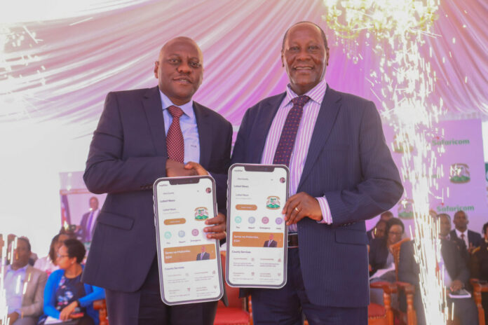 From Left, Safaricom PLC Chief Corporate Security Officer Nicholas Mulila and the Governor of Kitui County H.E Dr. Julius Malombe hold a dummy phone app of the new myKutuicounty App launched at the county headquarters in Kitui County today. Kitui county becomes the second county in the Eastern Region to launch the digitisation of its services through the app. The app will help the county manage their revenue and reach out to most of its residents - Bizna Kenya